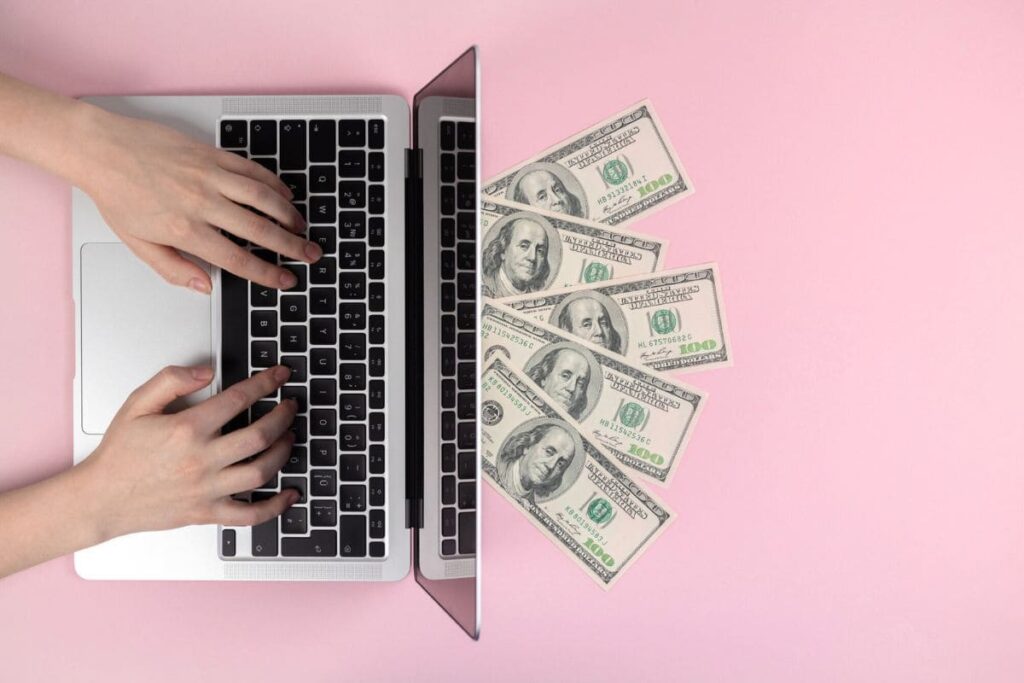 A woman using a laptop, with cash on the desk for blog post sign up and get free money