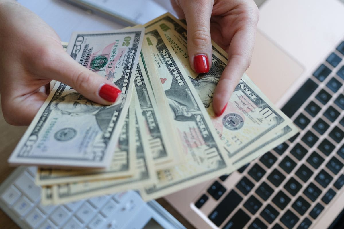 Closeup image of a woman's hands counting cash while using a laptop for blog post sign up and get free money