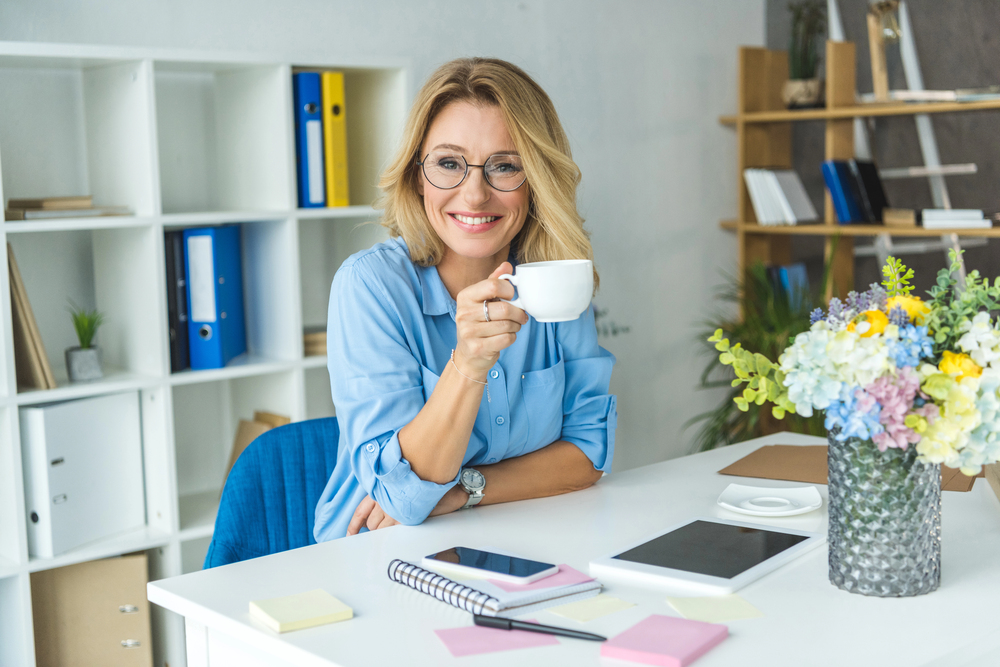 A woman drinking a cup of coffee in her home office working her high-paying job