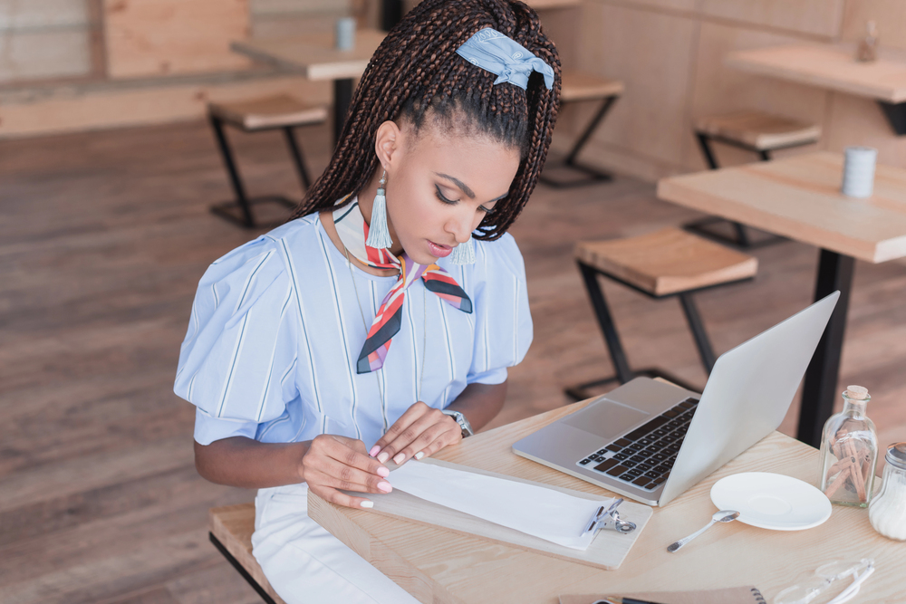 A young woman with long braided hair looking over her notes about different AI side hustles