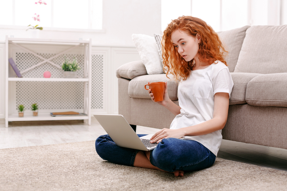 A young woman with long wavy red hair reading a MyPoints review on her laptop