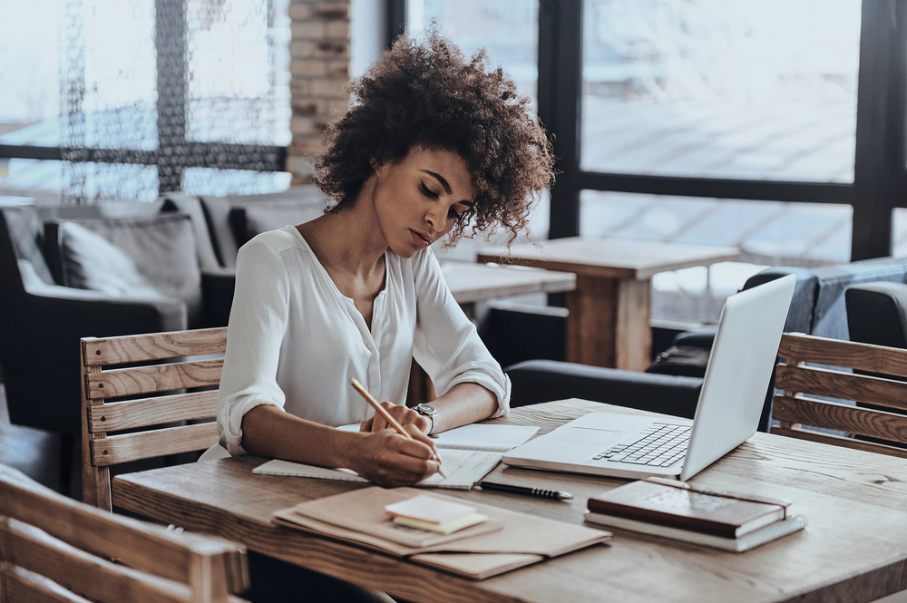 A young woman writing in a notebook looking for online jobs for writers