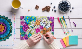 Overhead view of a woman using colored pencils to color a design in an adult coloring book for blog post get paid to color.