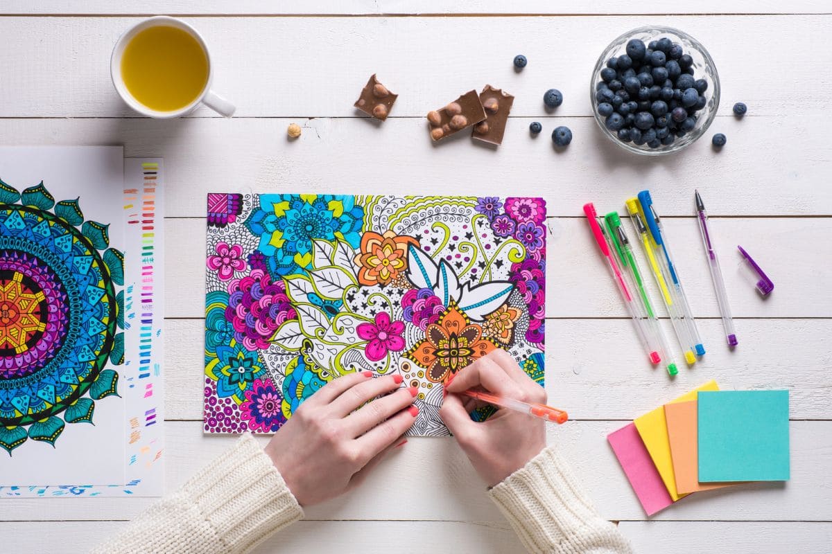 Overhead view of a woman using colored pencils to color a design in an adult coloring book for blog post get paid to color.