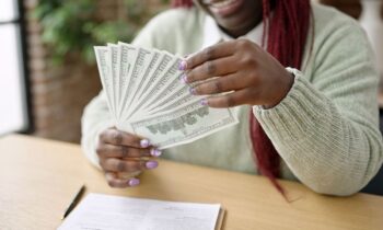 A woman sitting at her home office desk, counting cash and writing in a notebook for $10K a month