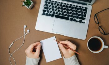 A woman working on updating her resume, using a laptop and writing in a notepad.