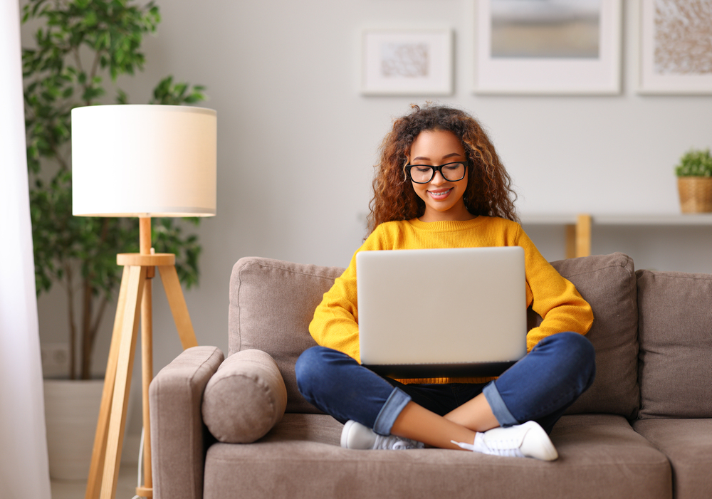 Young female sitting on the sofa looking at her laptop looking for work from home jobs for teens