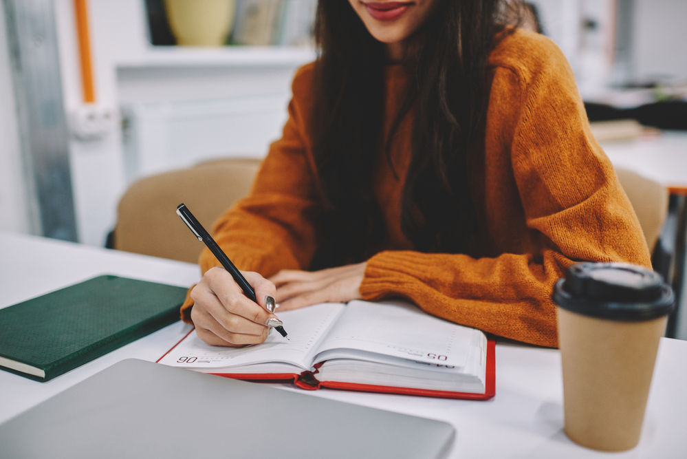 Woman writing in her notebook planning out her paid writing jobs
