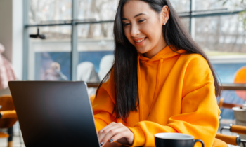 Young woman with long hair sitting in a cafe working on her laptop looking for remote facebook jobs